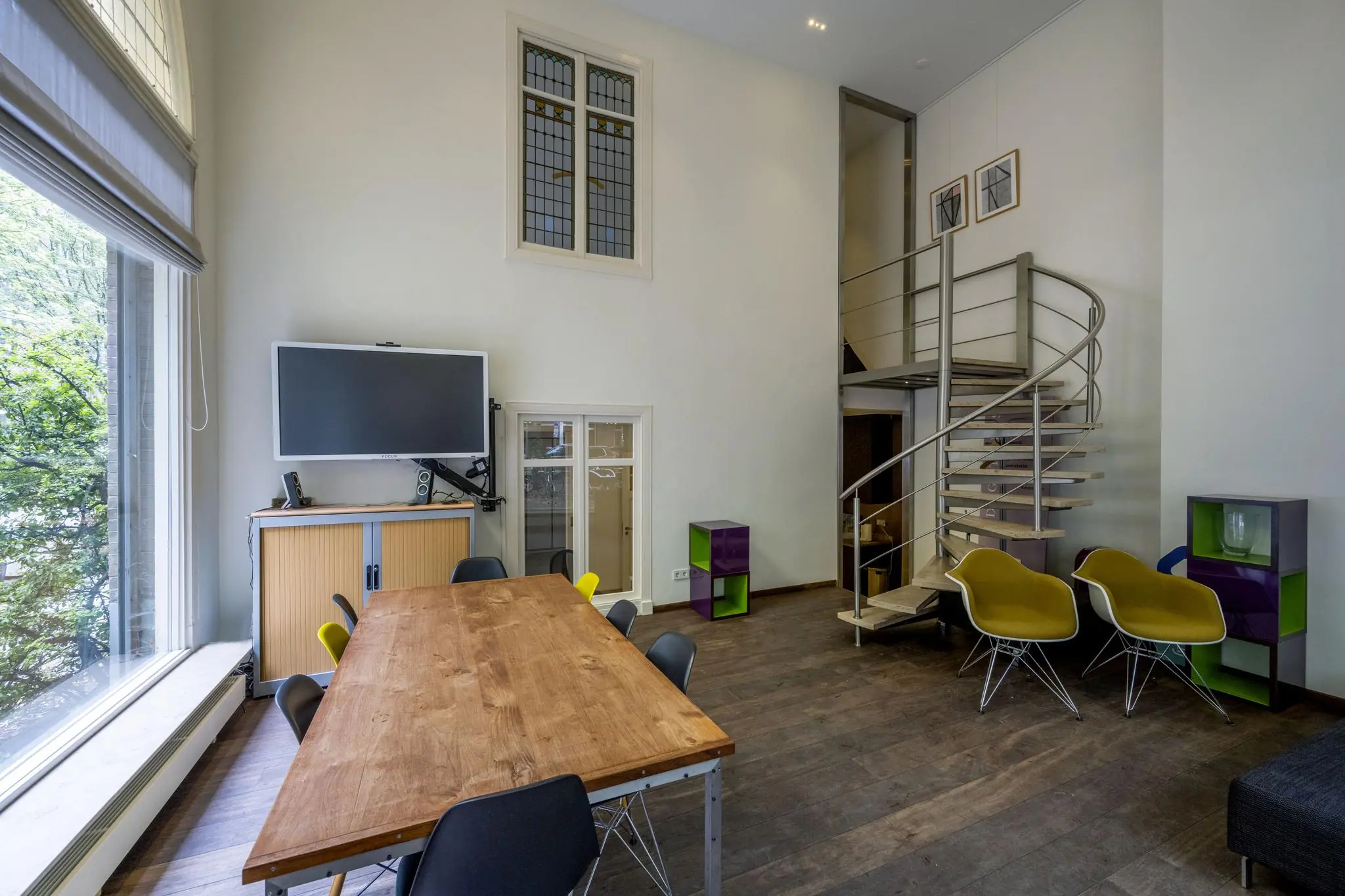 Moderne vergaderruimte aan de Lomanstraat met houten tafel, grote ramen, wenteltrap en flatscreen-tv.