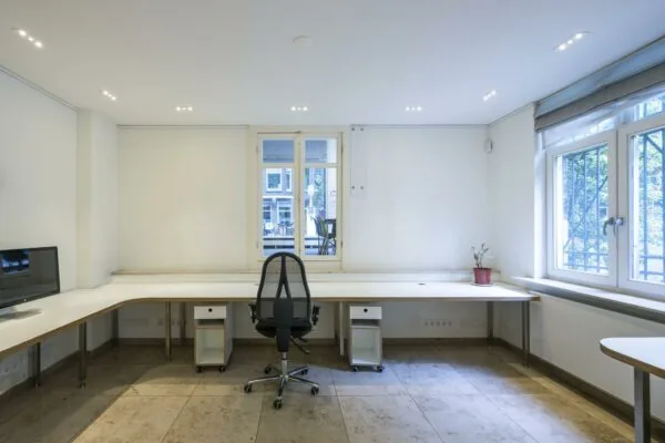 Lichte en minimalistische kantoorruimte aan de Lomanstraat met een groot hoekbureau, bureaustoel, plant en raam met uitzicht op de straat.