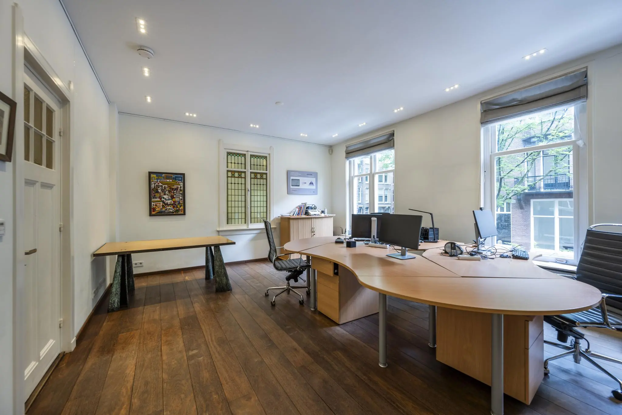 Modern kantoor met houten vloer, grote ramen en meerdere werkplekken aan een gebogen bureau op de Lomanstraat.