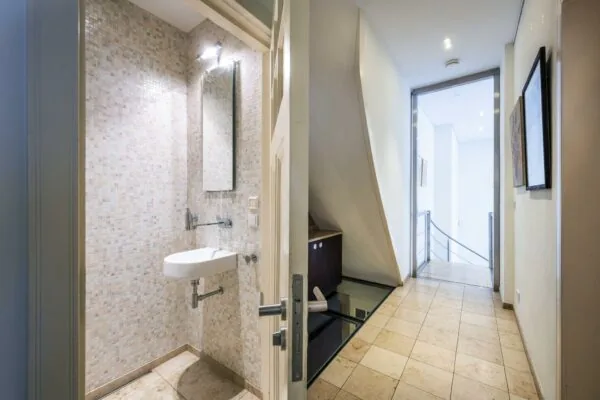 Moderne gang met een open deur naar een kleine toiletruimte met mozaïektegels en een zwevend fonteintje.