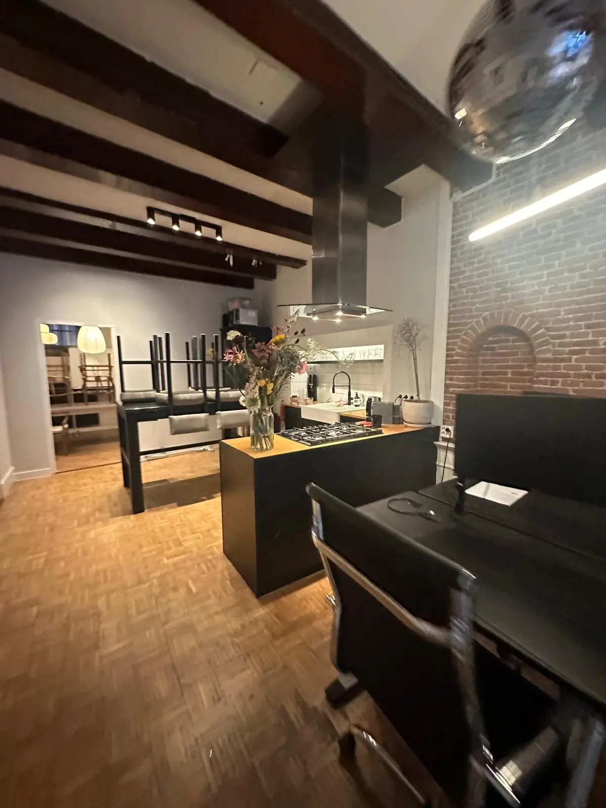 Moderne keuken en werkruimte met houten balkenplafond aan de Herengracht, met een kookeiland, bloemenvaas en bakstenen muur.