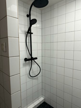 Moderne inloopdouche met witte tegels en een zwarte regendouche in een badkamer aan de Herengracht.