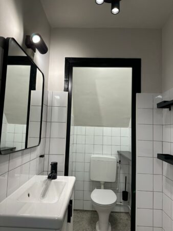 Moderne, zwart-wit betegelde toiletruimte met wastafel, spiegel en hanglampen aan het plafond.