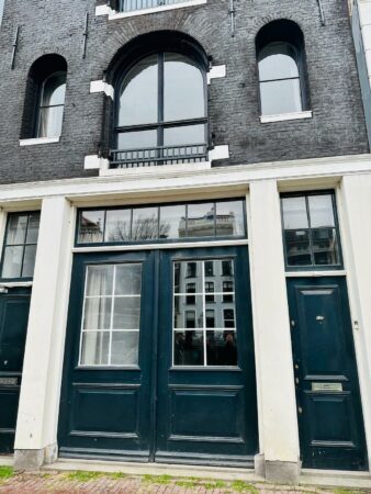 Voorgevel van een zwart bakstenen pand aan de Herengracht met hoge zwarte deuren en grote ramen.
