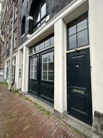 Voorgevel van een gebouw aan de Herengracht met zwarte deuren en witte kozijnen.