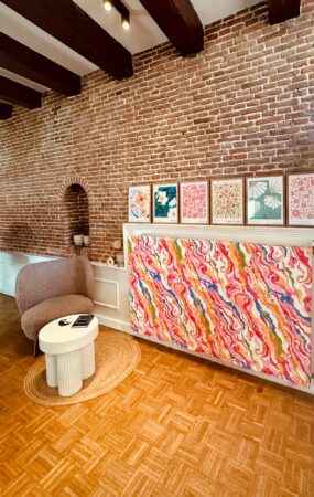 Stijlvol interieur met een kunstzinnige, kleurrijke wanddecoratie en posters van wereldsteden tegen een bakstenen muur.