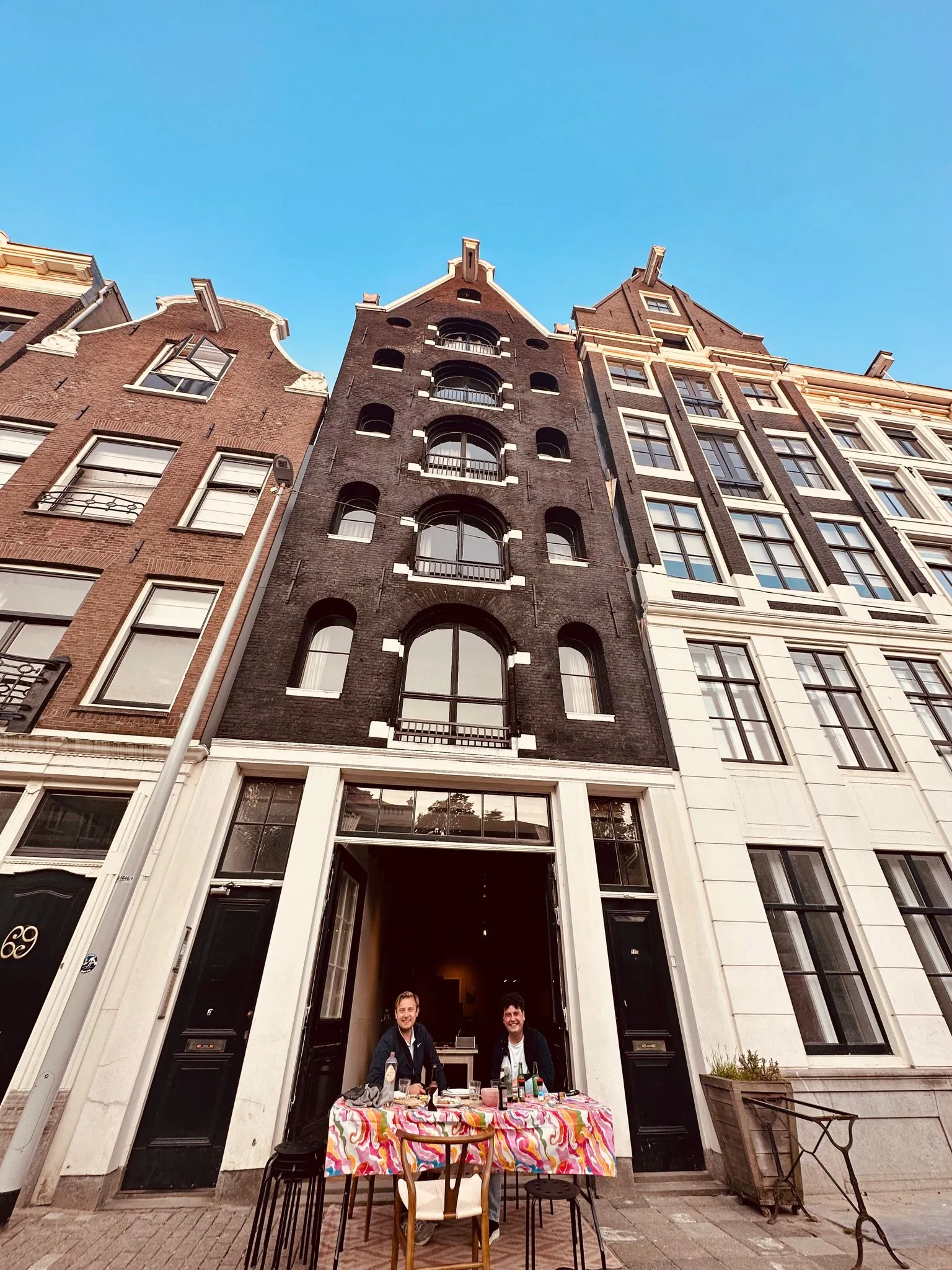 Twee mensen zitten aan een gedekte tafel voor een historisch grachtenpand aan de Herengracht in Amsterdam.
