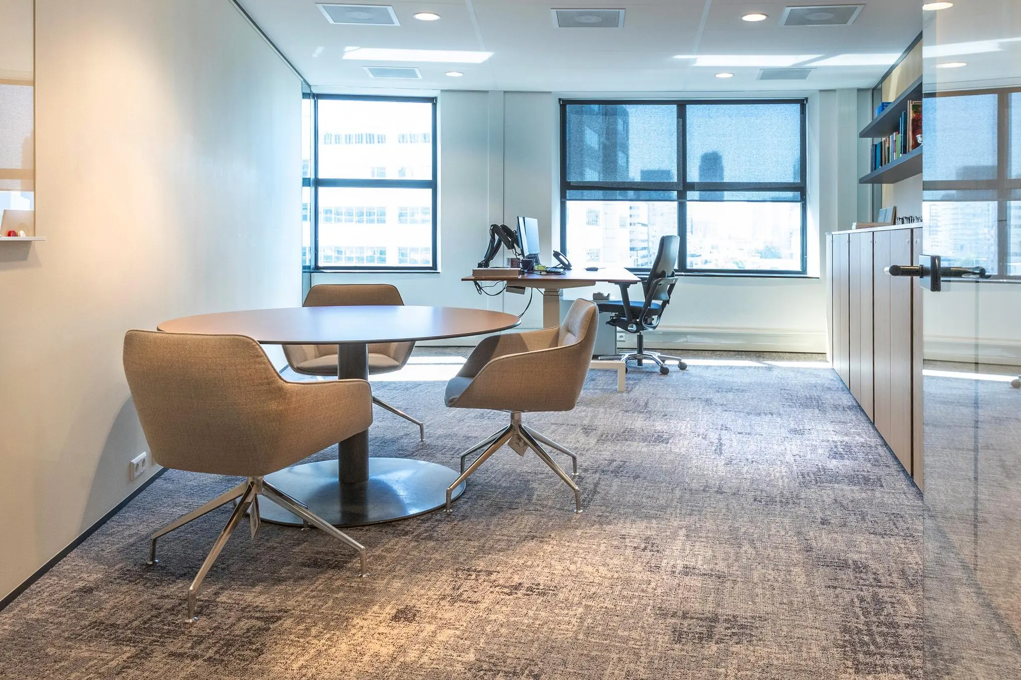 Modern kantoorinterieur aan het Weena met een ronde vergadertafel, vier stoelen en een werkplek bij het raam.