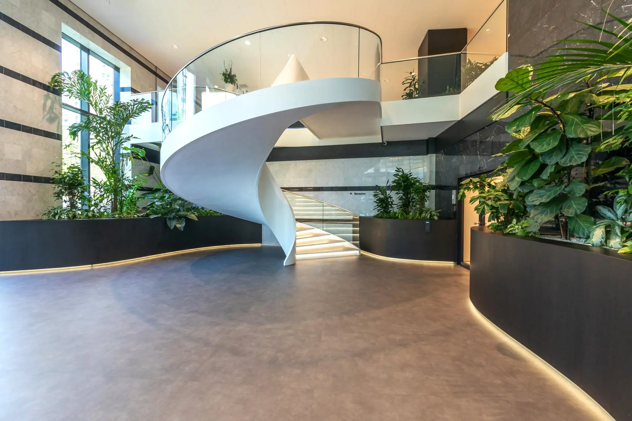 Moderne kantoorlobby aan het Weena met een witte wenteltrap, grote plantenbakken en strakke verlichting.