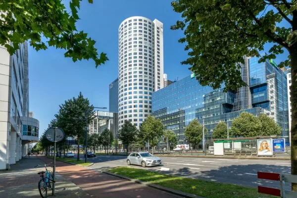 Straatbeeld van de Weena in Rotterdam met moderne kantoorgebouwen, waaronder een rond wit gebouw en een glazen gevel.