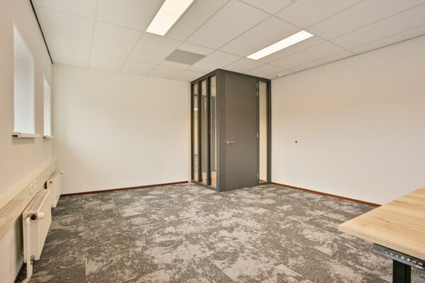 Leeg modern kantoor met grijze deur, glazen panelen en grijs gemêleerd tapijt.