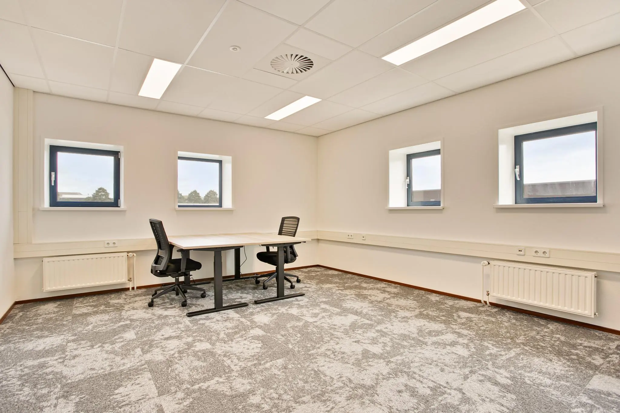 Licht en modern kantoor met twee bureaustoelen, een bureau en vier ramen.