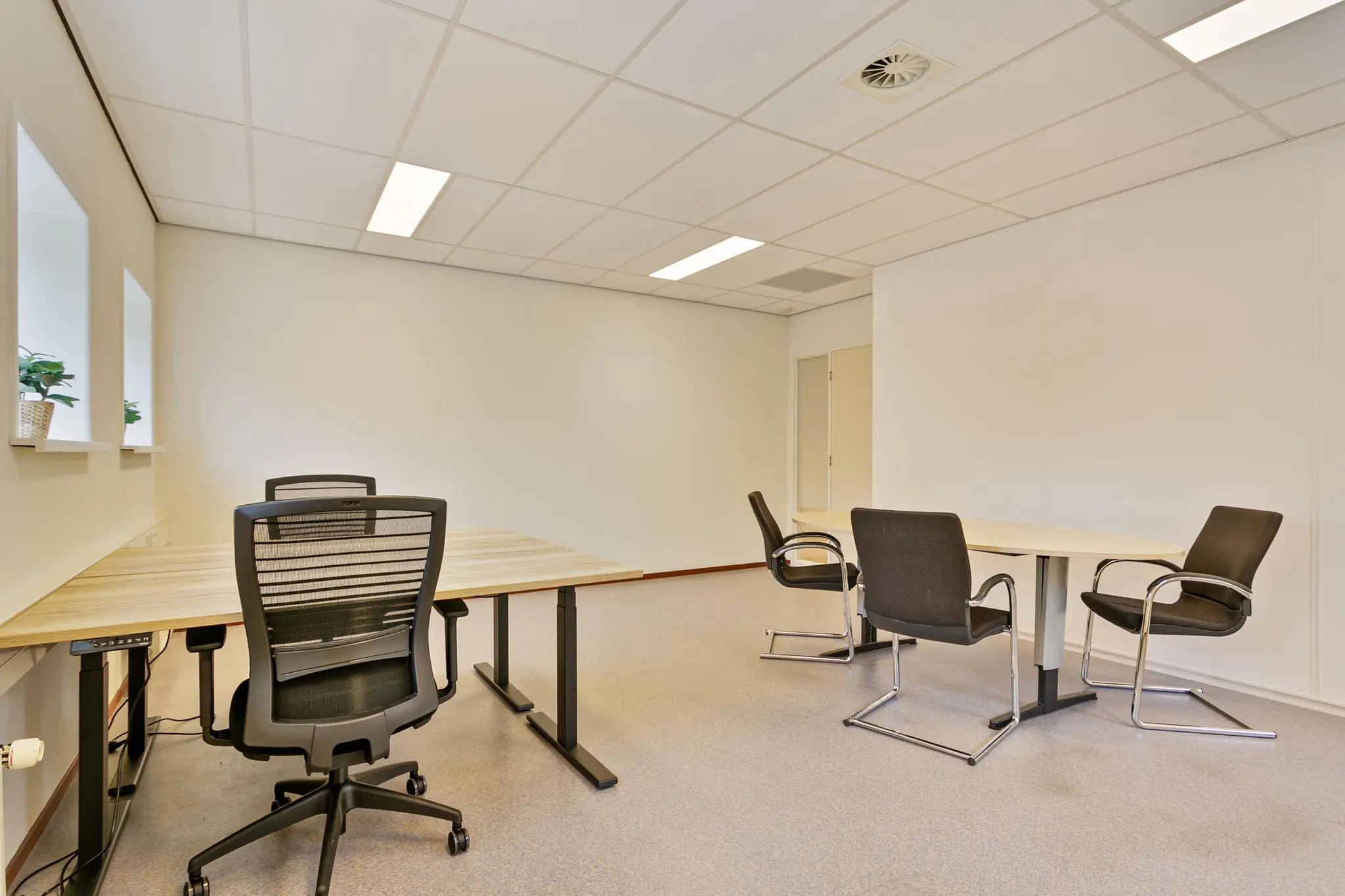 Kantoorruimte met twee bureaus, bureaustoelen en een vergadertafel met vier stoelen in een lichte, moderne setting.