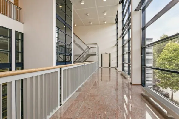 Licht en modern trappenhuis met grote glazen gevel en glanzende marmeren vloer.