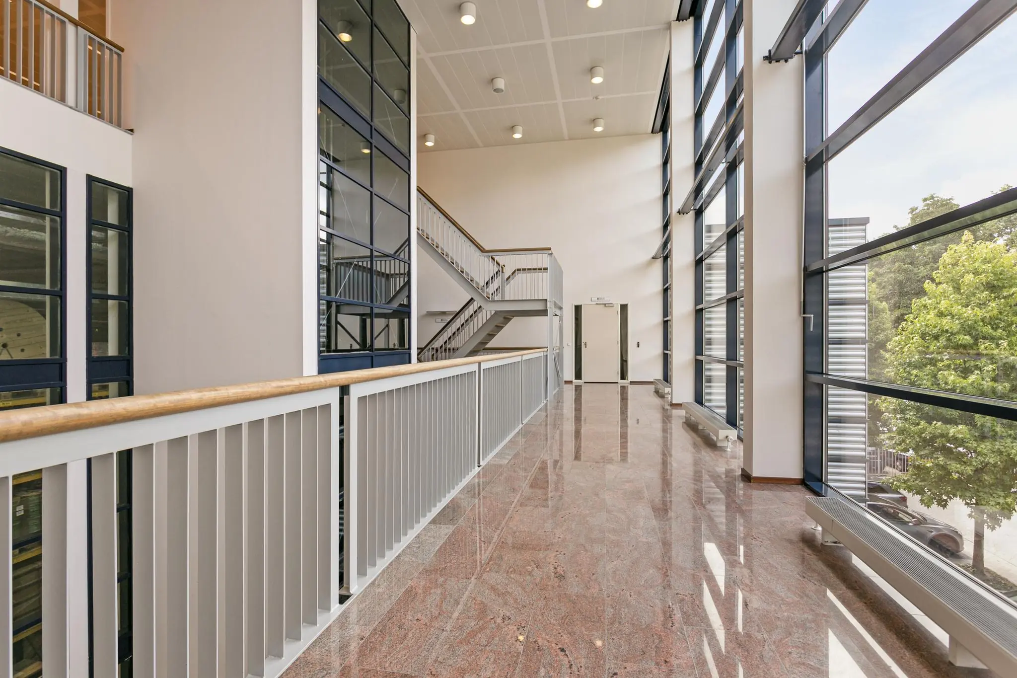 Licht en modern trappenhuis met grote glazen gevel en glanzende marmeren vloer.