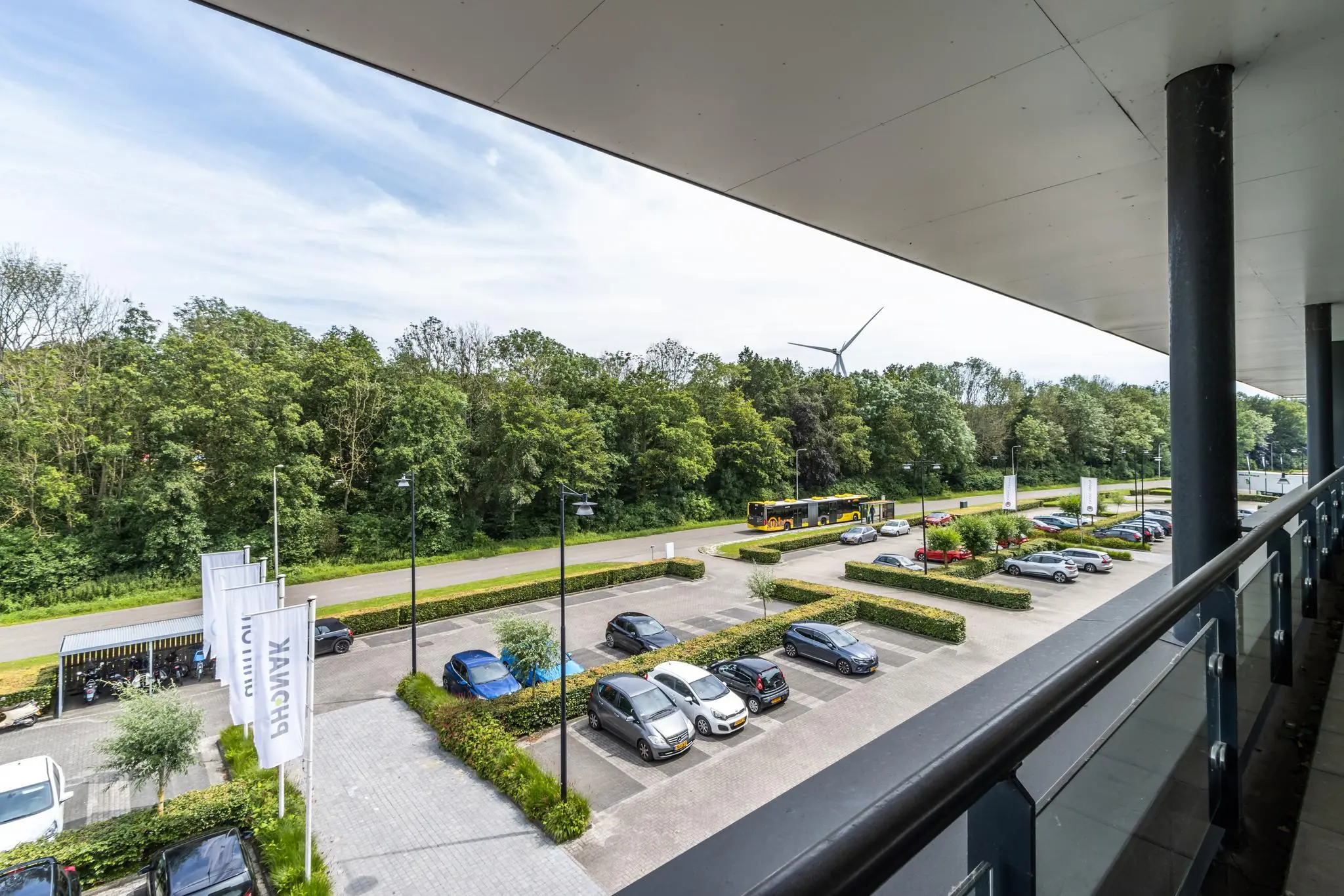 Parkeerterrein aan de Laanakkerweg met geparkeerde auto's, een passerende bus en zicht op een windmolen en bomen.