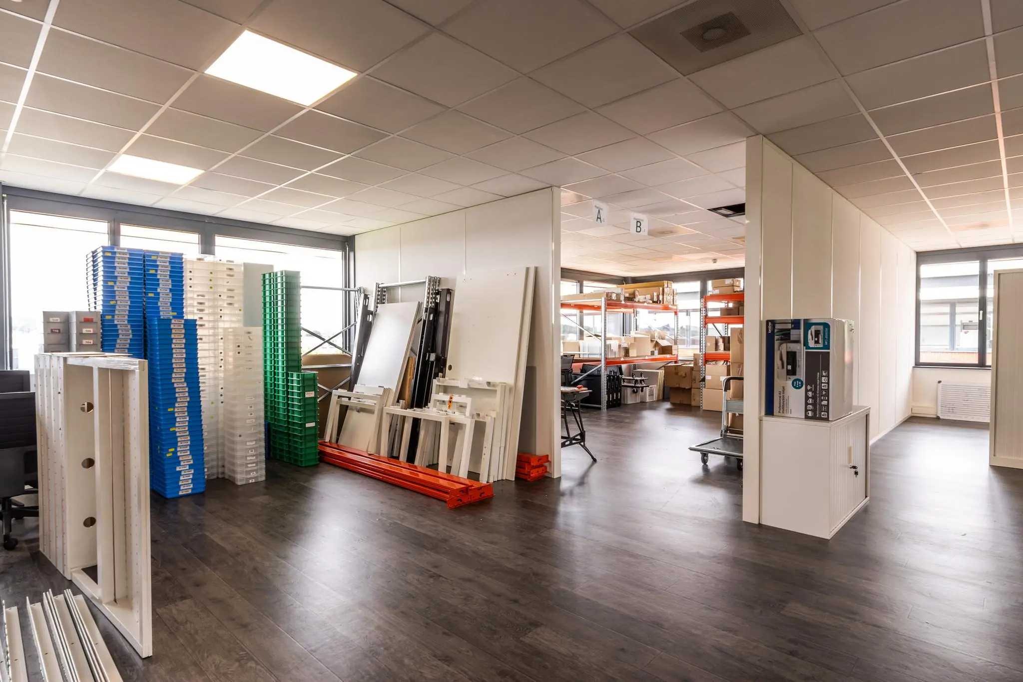 Interieur van een bedrijfsruimte aan de Laanakkerweg met stapels kunststof bakken, metalen rekken en bureaus in een open opslag- en werkruimte.