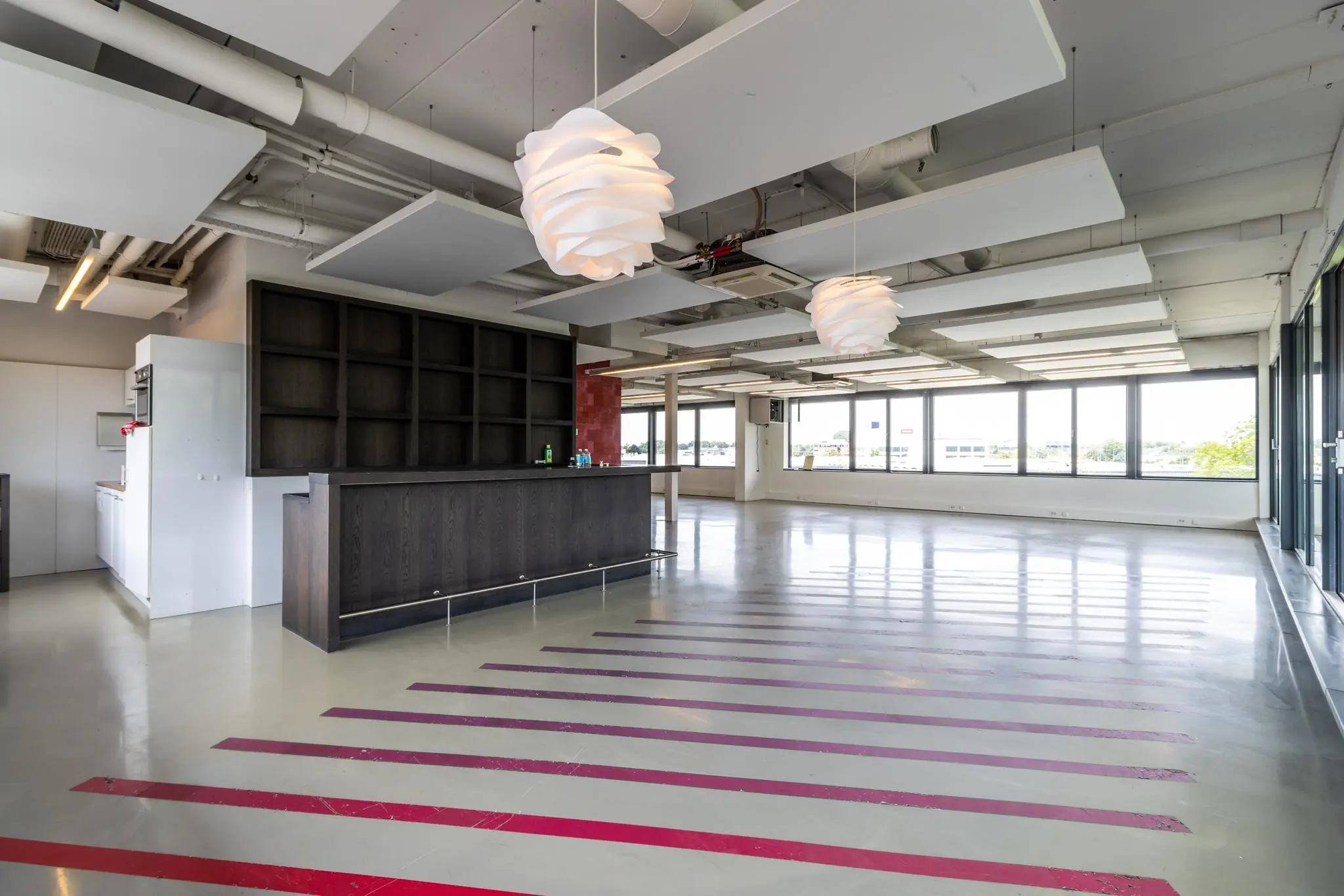 Moderne, open kantoorruimte aan de Laanakkerweg met een bar, opvallende plafondlampen en grote raampartijen.