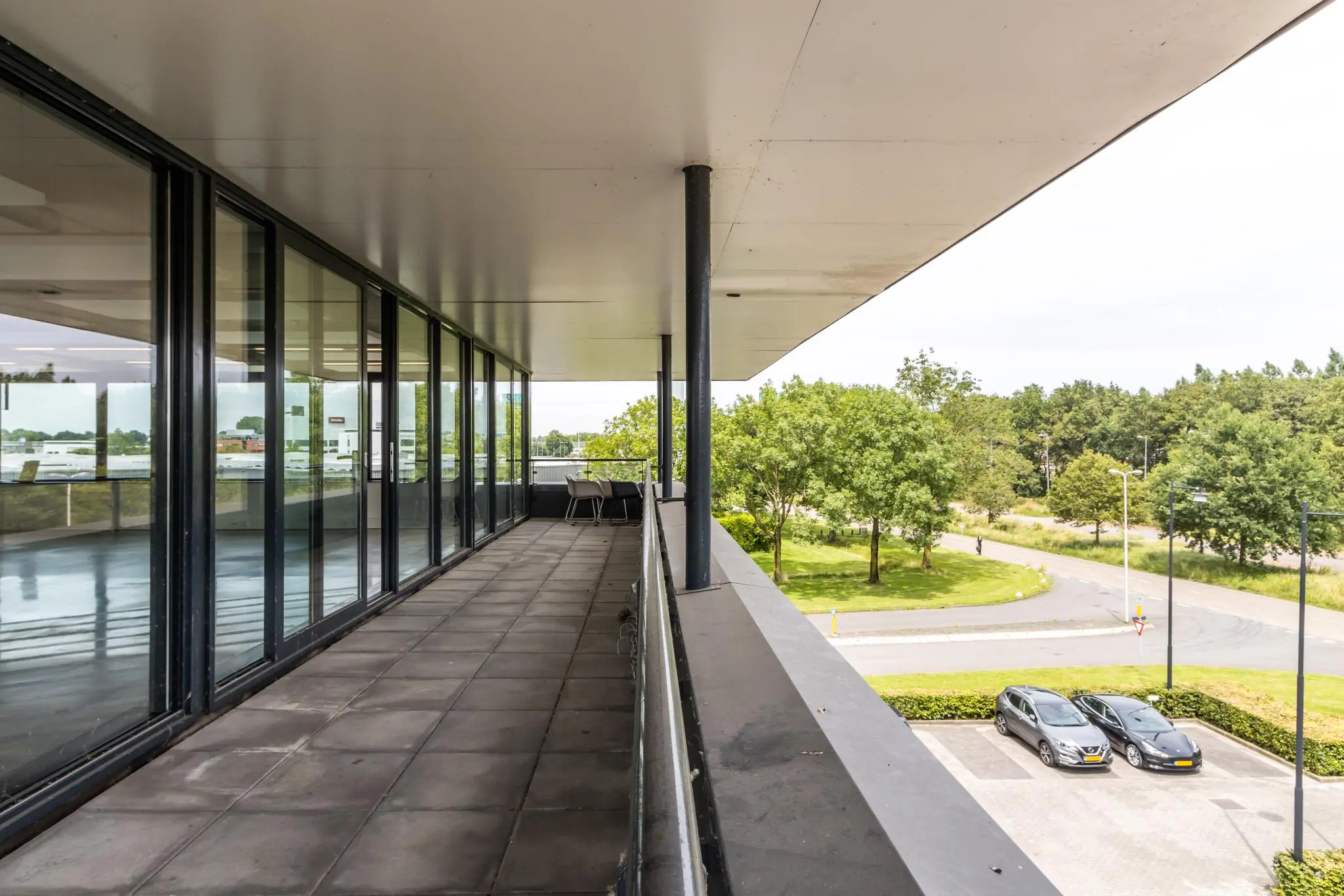 Balkon van een kantoorpand aan de Laanakkerweg met uitzicht op parkeerplaatsen en groenvoorziening.