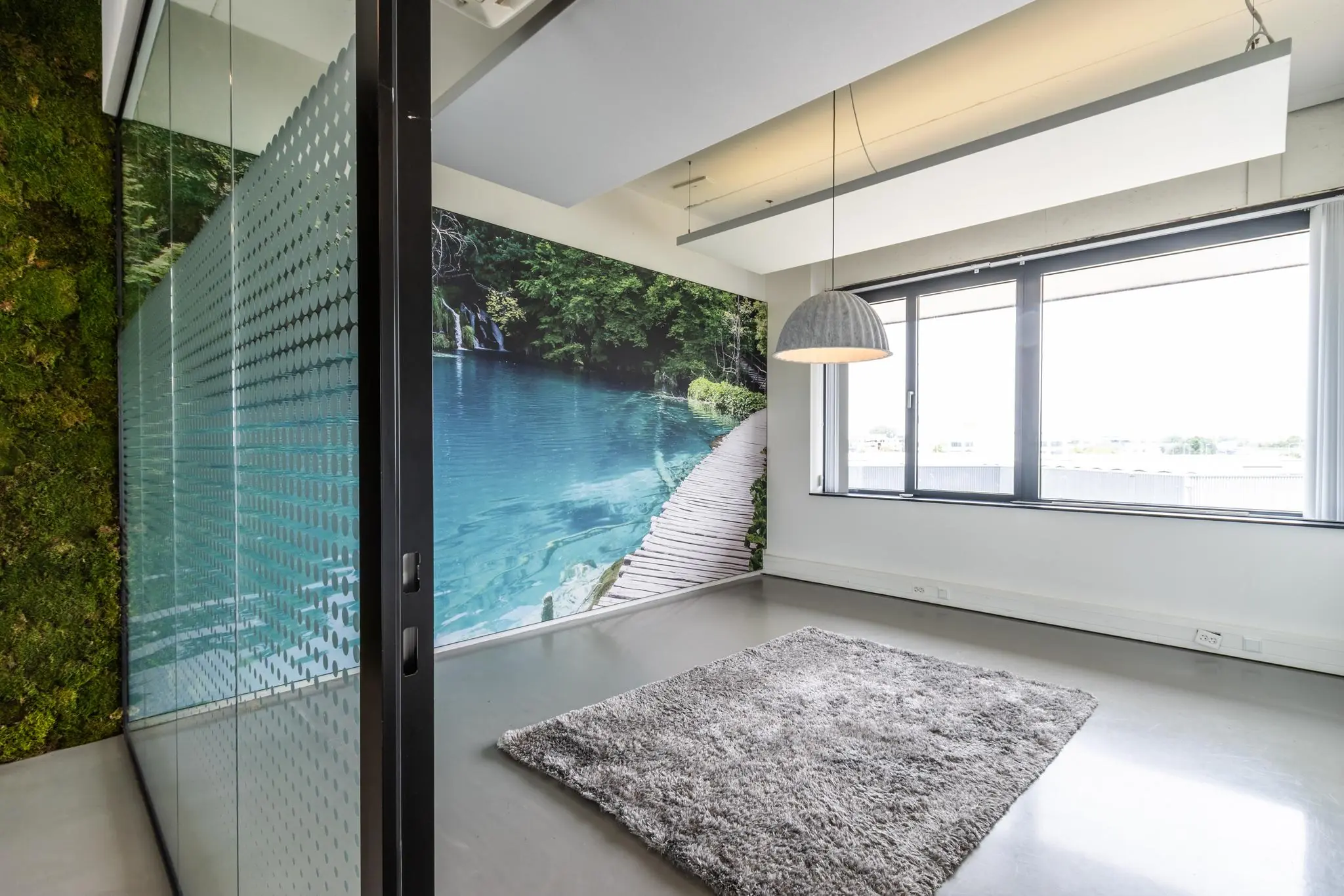 Modern kantoorinterieur aan de Laanakkerweg met een natuurmuur, groot raam en fotobehang van een meer met vlonderpad.