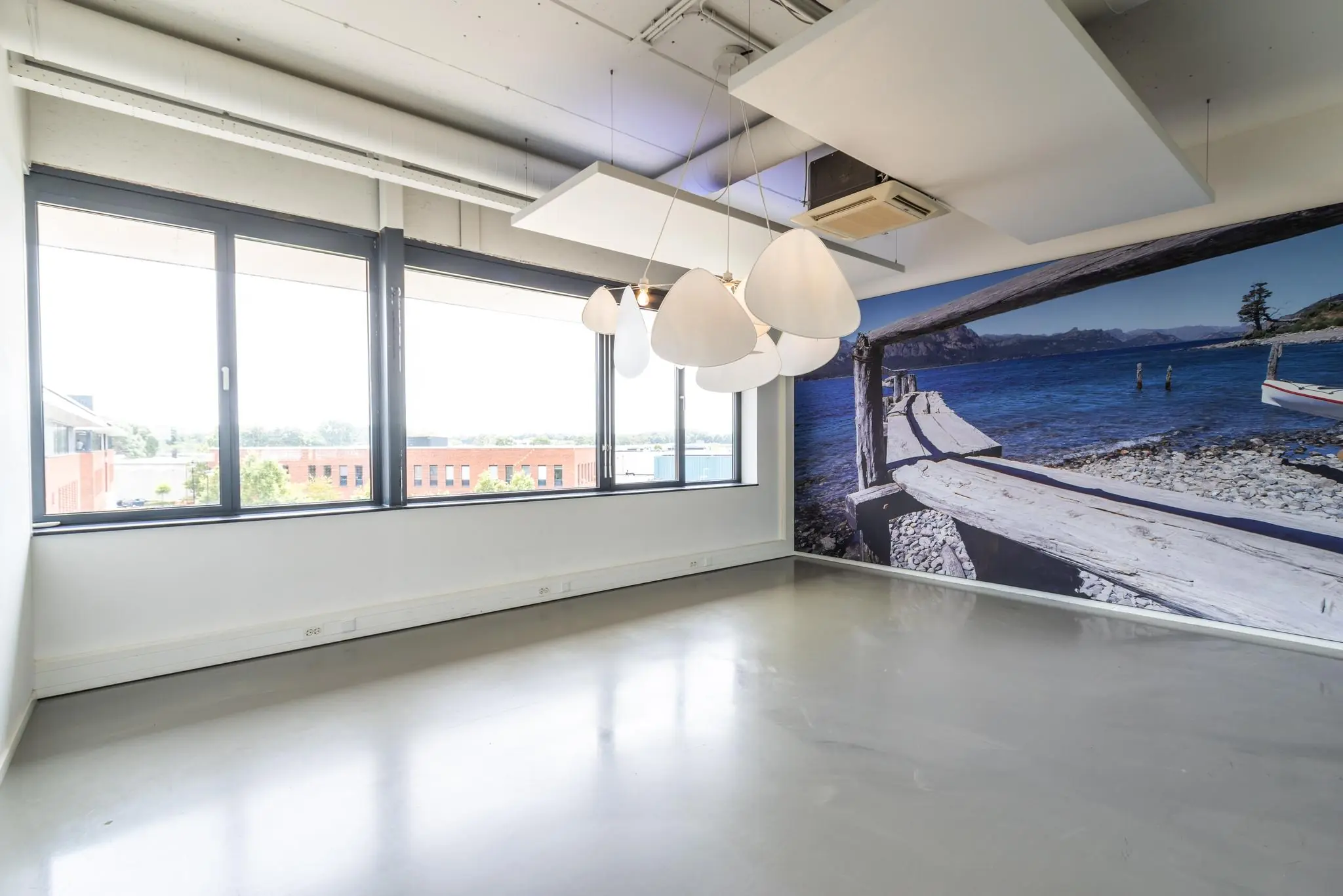 Lichte, lege kantoorruimte aan de Laanakkerweg met grote ramen, moderne verlichting en een wand met een fotoprint van een steiger aan een meer.