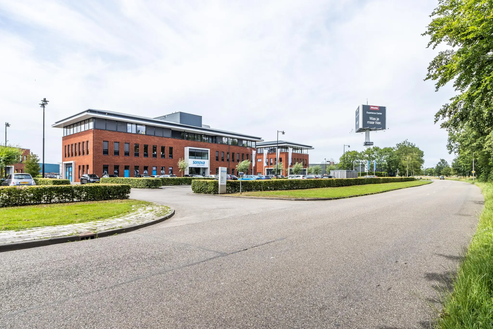 Kantoorgebouw van Sonova aan de Laanakkerweg met parkeerplaats en reclamezuil langs een rustige straat.