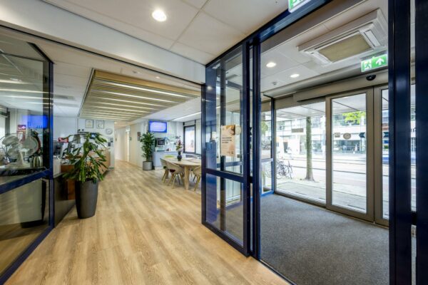 Moderne entree en wachtruimte van een kantoorpand aan de Sarphatistraat met houten vloer, glazen deuren en ontvangstbalie.