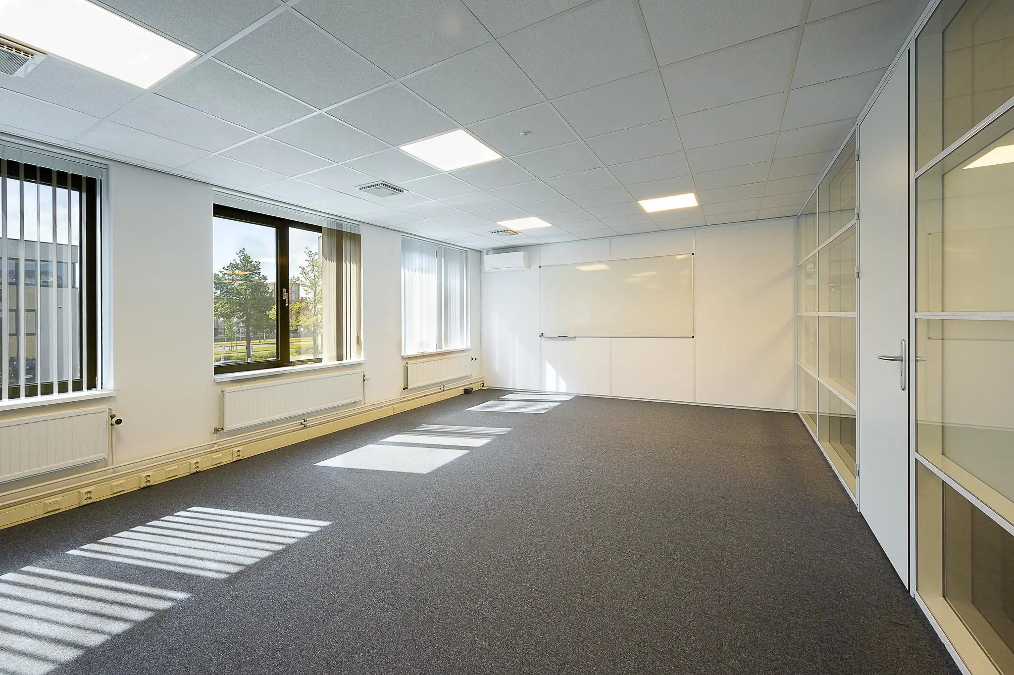 Lichte, lege kantoorruimte aan de Ligusterbaan met ramen, systeemplafond en whiteboard.