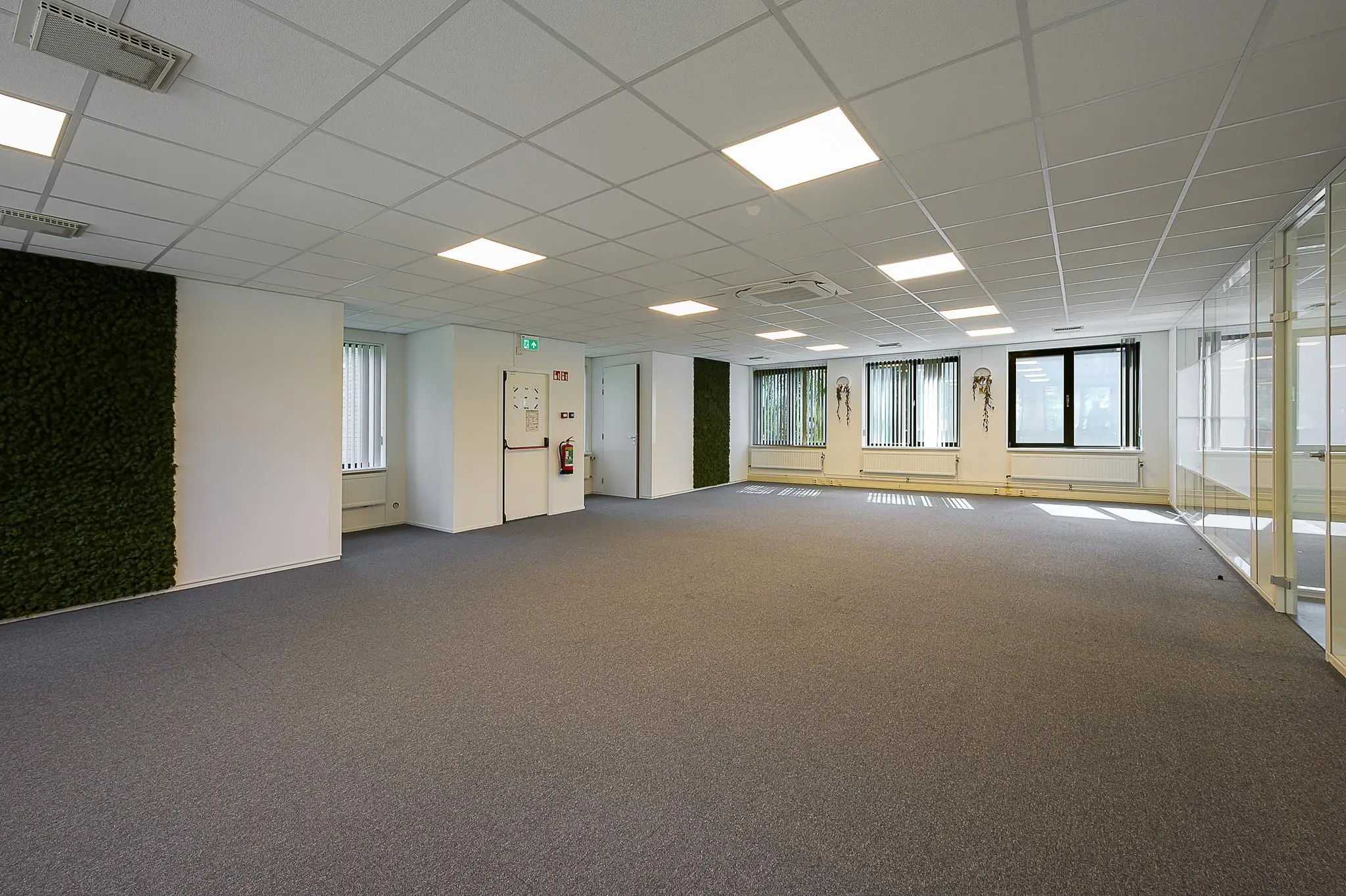 Ruime, lege kantoorgruimte aan de Ligusterbaan met systeemplafond, tapijtvloer en grote ramen met verticale jaloezieën.