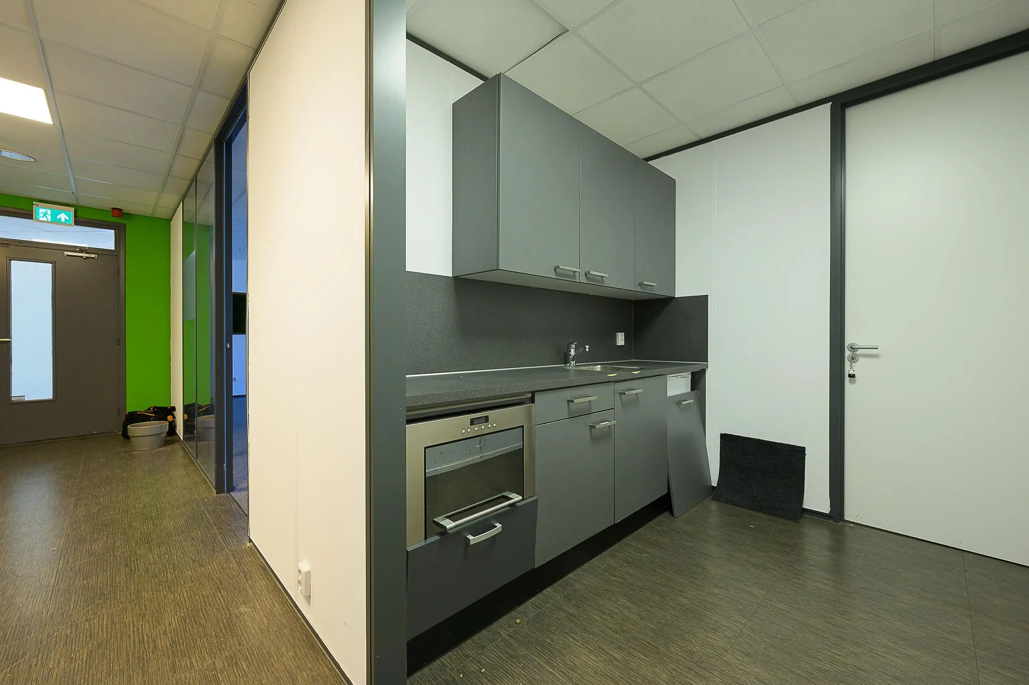 Keukenhoek met grijze keukenkastjes en een oven in een kantoorruimte aan de Ligusterbaan.