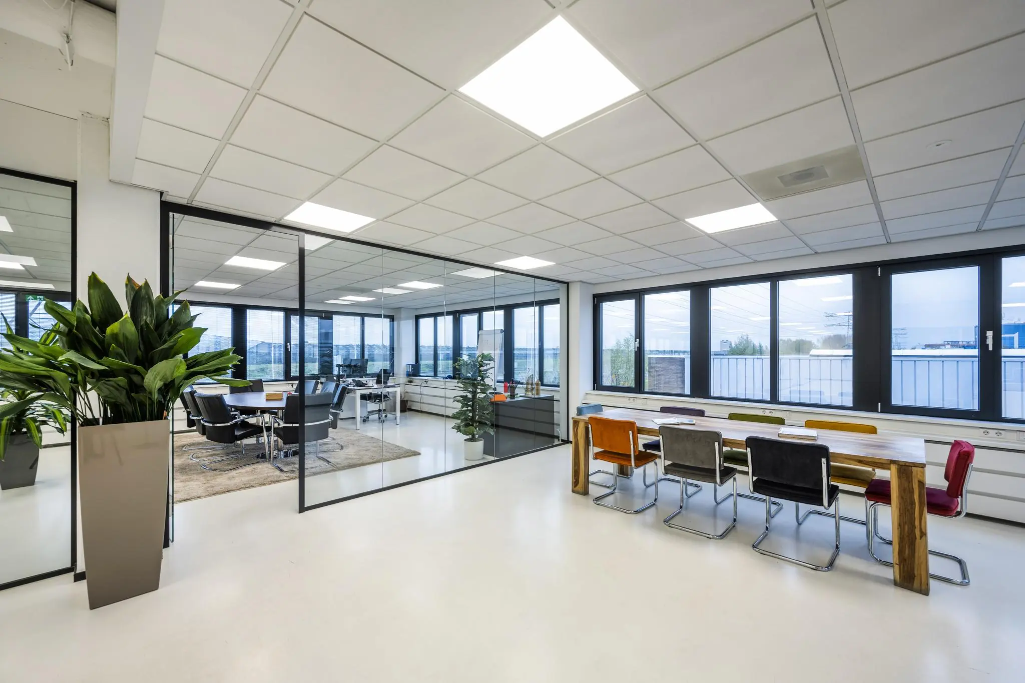 Modern kantoorinterieur aan de Savannahweg met glazen vergaderruimte, lange houten tafel en kleurrijke stoelen.
