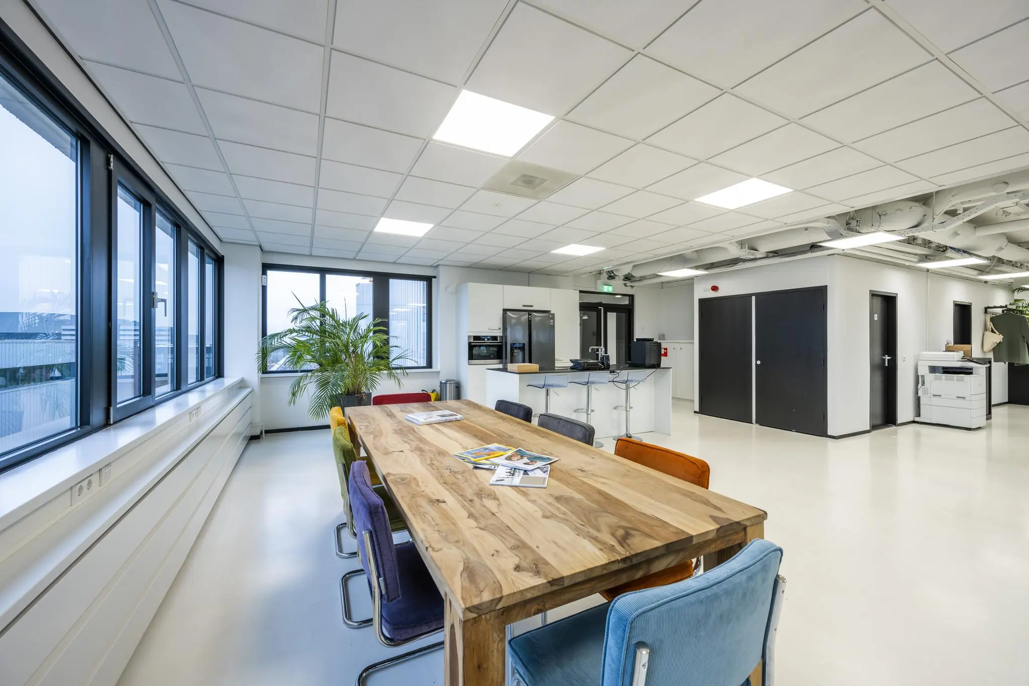 Moderne kantoorruimte aan de Savannahweg met een houten vergadertafel, kleurrijke stoelen en een open keuken.