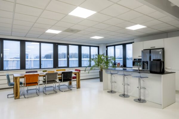 Moderne, licht ingerichte kantoorkeuken met een grote eettafel, barkrukken en uitzicht op de omgeving aan de Savannahweg.