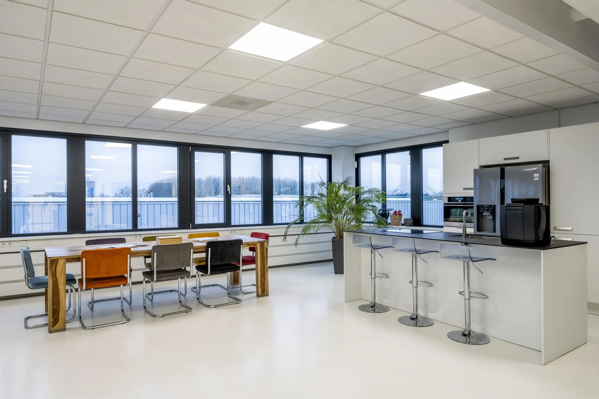 Moderne, licht ingerichte kantoorkeuken met een grote eettafel, barkrukken en uitzicht op de omgeving aan de Savannahweg.