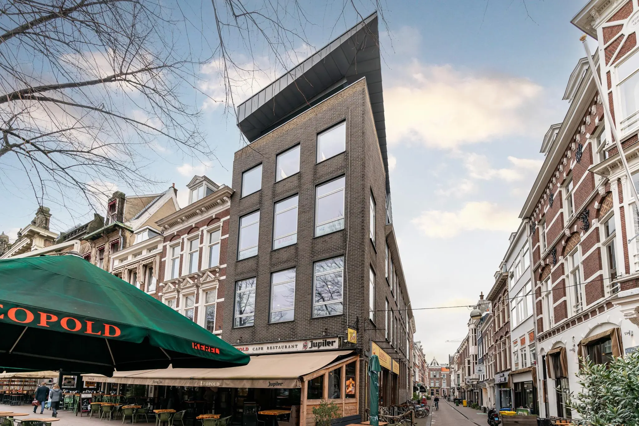 Straatbeeld met een modern hoekpand en café-restaurant Leopold aan het Plein in een historische binnenstad.