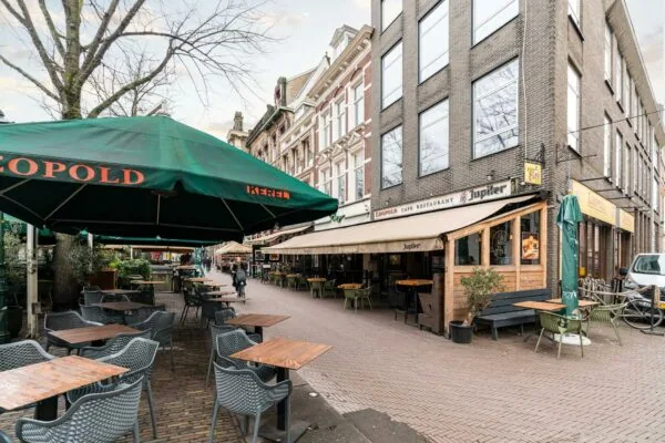 Terras van Café Restaurant Leopold aan een gezellig plein met tafels, stoelen en groene parasols.