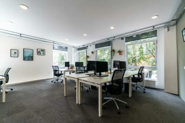 Moderne en lichte kantoorruimte met meerdere werkplekken, bureaustoelen en grote ramen met uitzicht op groen.