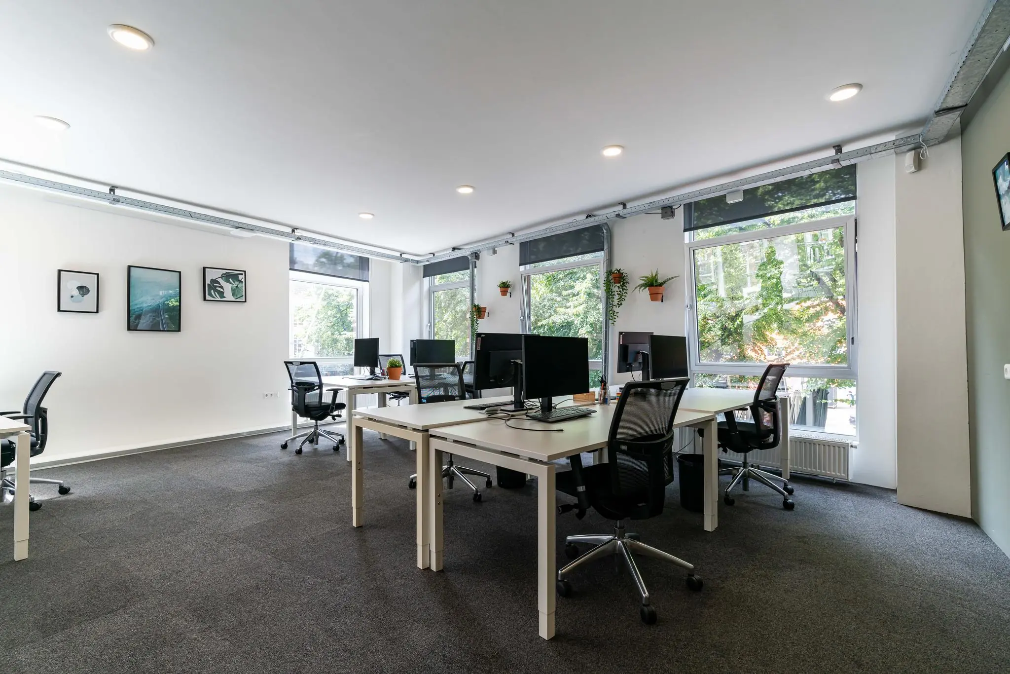 Moderne en lichte kantoorruimte met meerdere werkplekken, bureaustoelen en grote ramen met uitzicht op groen.