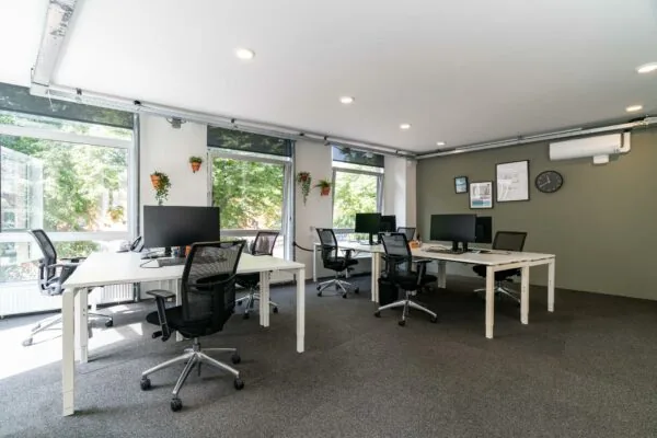 Modern, licht kantoor met meerdere werkplekken, bureaustoelen en grote ramen met uitzicht op groen.