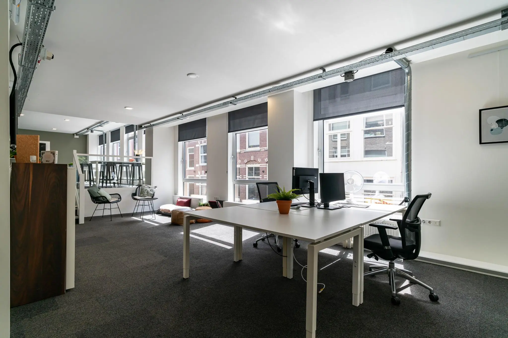 Modern ingericht en licht kantoor met werkplekken, zitgedeelte en grote ramen met uitzicht op het plein.