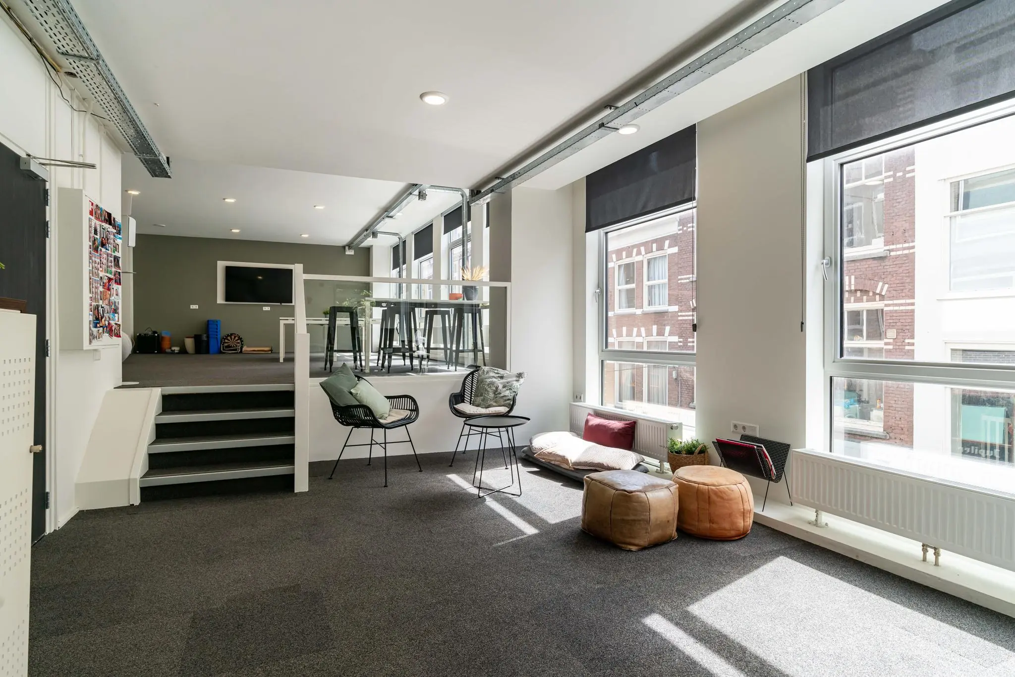 Licht en modern kantoorinterieur met zithoek, hoge ramen en een verhoogd werkplatform.