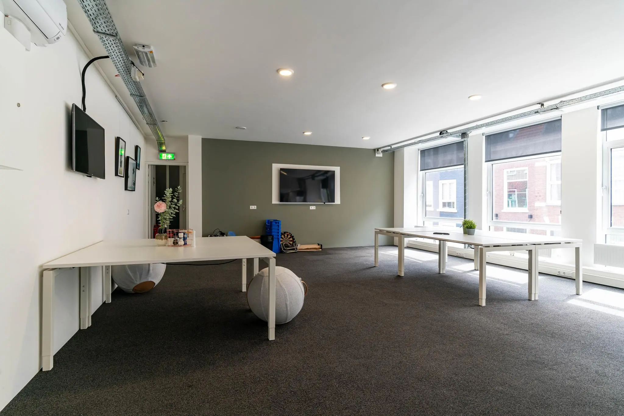 Moderne, lichte kantoorruimte met witte bureaus, grote ramen en een muurtelevisie.