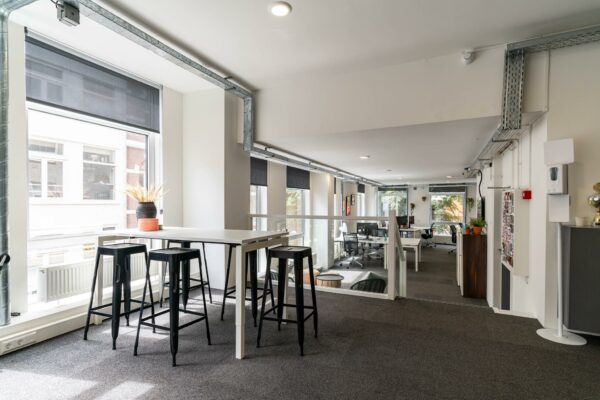 Moderne, lichte kantoorruimte met hoge tafels, barkrukken en werkplekken aan het raam.
