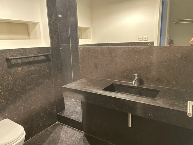 Moderne badkamer aan de Danzigerkade met donker natuurstenen wastafelblad, ingebouwde wasbak en grote spiegel.