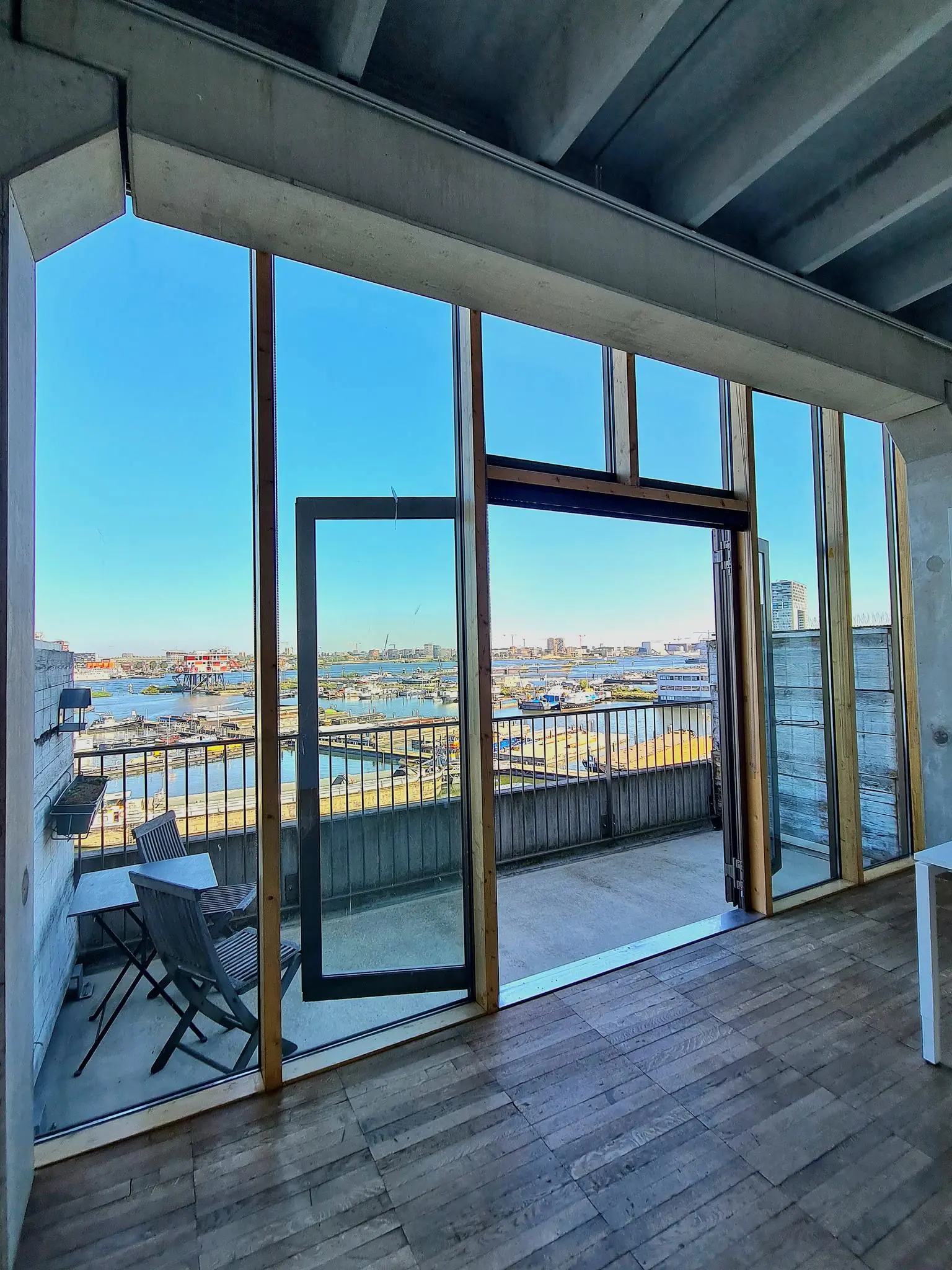 Uitzicht vanaf een appartement aan de Danzigerkade op een balkon met zitplek en de haven van Amsterdam op de achtergrond.