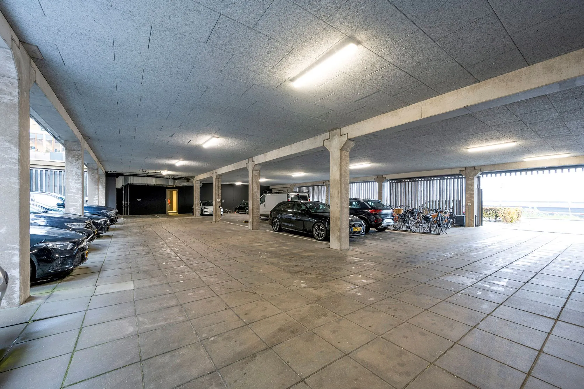 Overdekte parkeergarage aan de Danzigerkade met geparkeerde auto's, fietsen en betonnen zuilen.