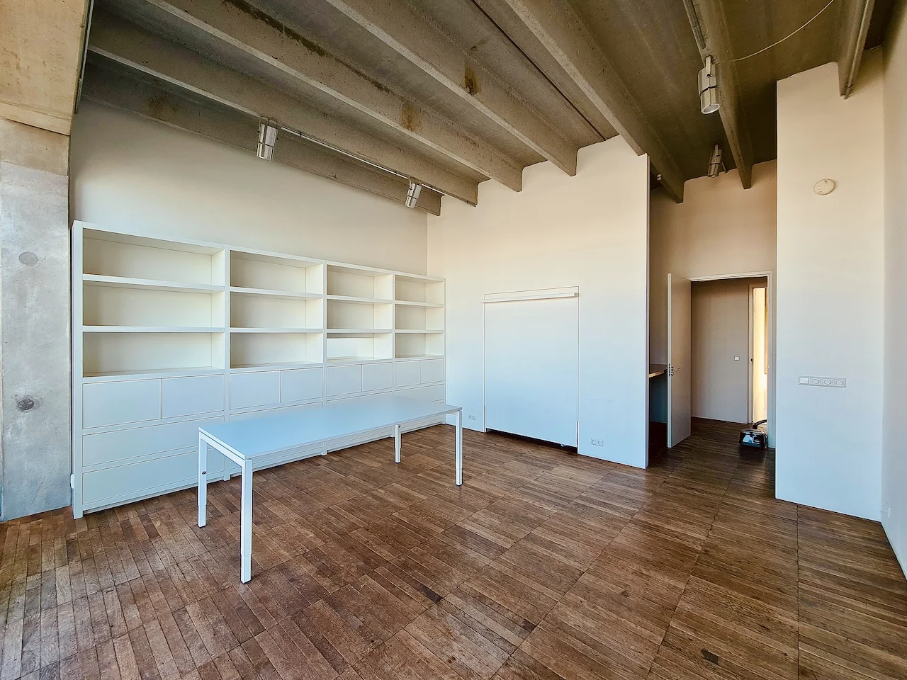 Lichte, industrieel ogende ruimte aan de Danzigerkade met houten vloer, hoge plafonds, witte boekenkasten en een minimalistisch bureau.