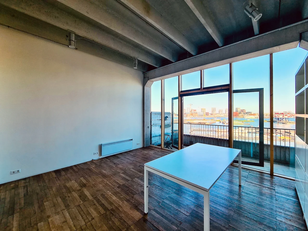 Lichte ruimte aan de Danzigerkade met houten vloer, betonnen plafond en uitzicht op het water en de skyline van Amsterdam.