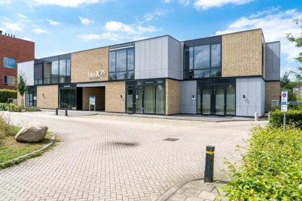 Modern kantoorgebouw genaamd bloX21 met de Ontwerpacademie en uitvaartcentrum De Boog aan een rustige straat.