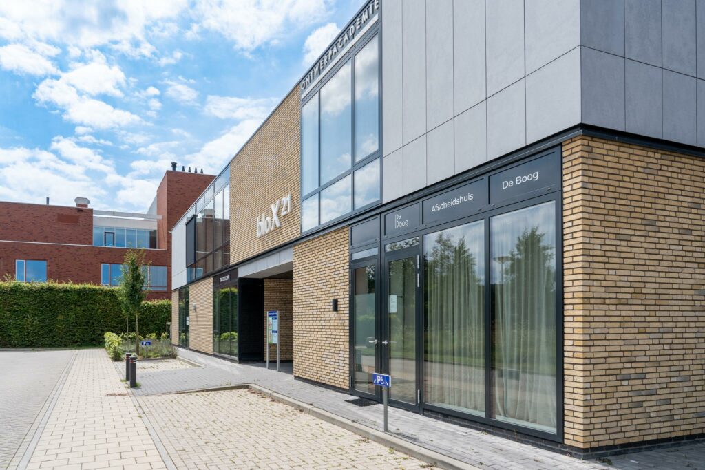 Moderne gevel van het gebouw HoX21 met het afscheids­huis De Boog aan de Handboog.